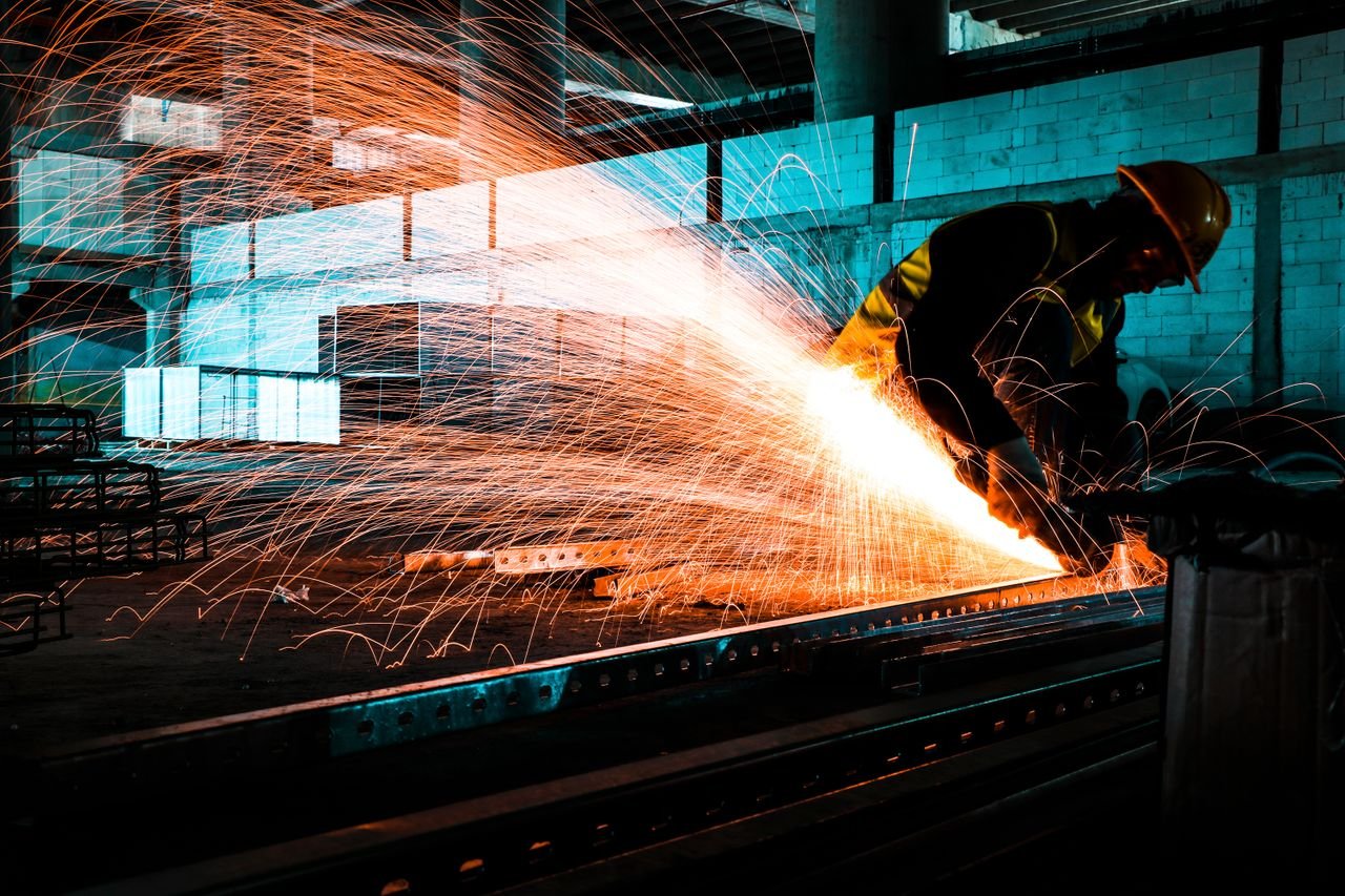 An industrial worker using an angle grinder to cut steel, creating bright sparks in a factory setting.